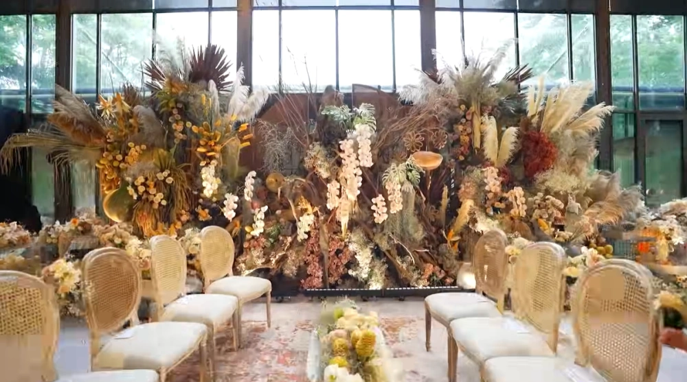 Tampilan Backdrop Utama Yang Menggunakan Panel Bertekstur Anyaman Dengan Dekorasi Rangkaian Bunga Kering [Sumber: Youtube]